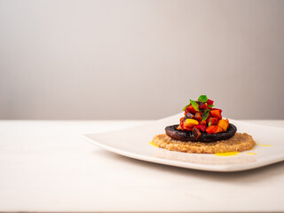 Ratatouille Stuffed Portobello Mushroom on Top of Creamy Quinotto with Olive Oil Sprinkles and Peppercorn served on Square White Plate