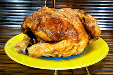 A roast chicken on yellow plate on wooden background.
