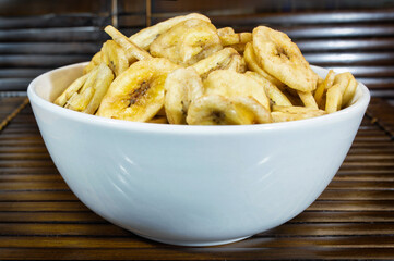 A full white bowl of banana chips on wooden background.