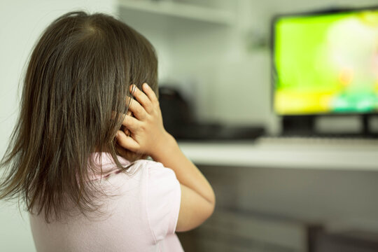 Little kid covering her ears, frightened from loud noise from TV. Autism.