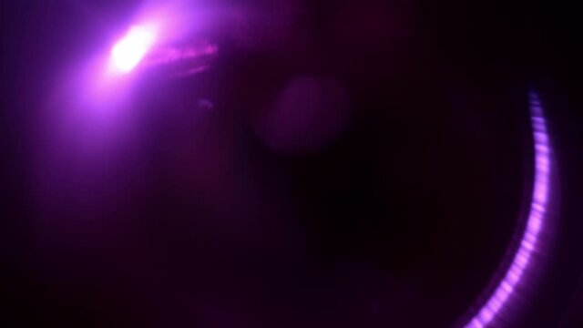 Round purple light transforms into pink and fades out in the dark. Lens flare transforms and spinning at the black background in the studio. The conception of light transitions and effects.