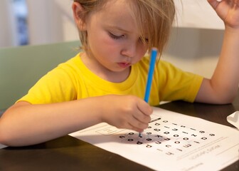 Naklejka premium A young kid doing school work at home. Learning words.