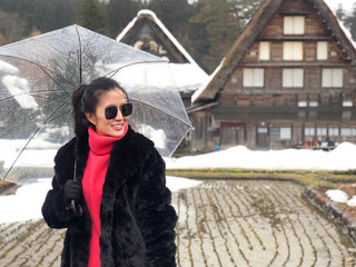 Woman tourist holding transparent umbrella in the winter and snow is falling at Shirakawago village at Gifu, Japan.
