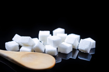 Closeup Macro Shot of White Cube Sugar Placed Bulk Along With Wooden Spoon. Against Black Background.