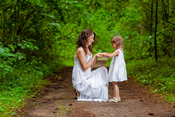 Naklejka na ściany i meble Young Caucasian Mother and Her Daughter Happily Playing Together Outdoors in Green Summer Forest.