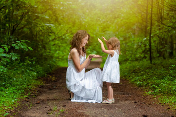 Naklejka na ściany i meble Young Caucasian Mother and Her Daughter Happily Playing Together Outdoors in Green Summer Forest.