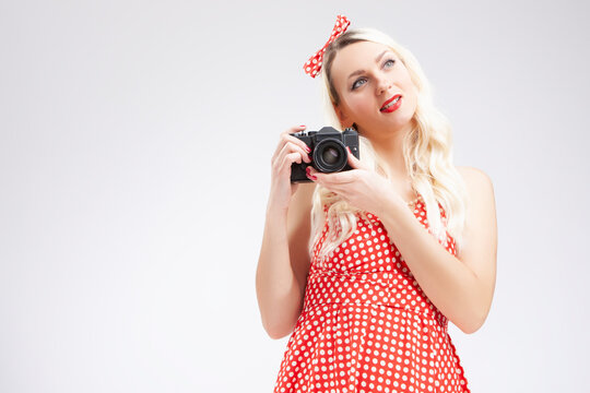 Pin-up Girl Concepts. Caucasian Blond Girl Posing in Pin-up Style and Holding Retro Film Camera in Hands. Against White.