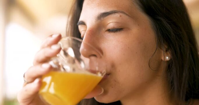 Authentic close up shot of an young brunette woman is drinking a fresh healthy dietetic biological natural orange juice from a transparent glass  taking a breakfast in the morning.