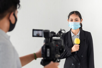 Fototapeta na wymiar Young asian woman journalist with medical mask and holding microphone working with Young asian man holding video camera reporting news of COVID-19 pandemic on white background.