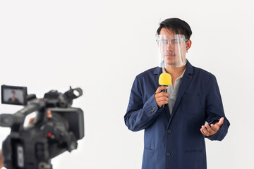 Young asian journalist man wearing face shield talking with microphone reporting news of COVID-19...