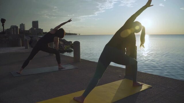 Women doing yoga by the water at sunrise. Slow motion.