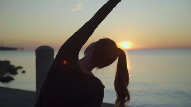 Silhouette of woman stretching beside lake at sunrise. Slow Motion.