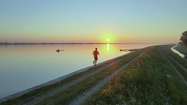 Runner jogging in the park close to the lake followed by a drone during a morning with an epic sunrise