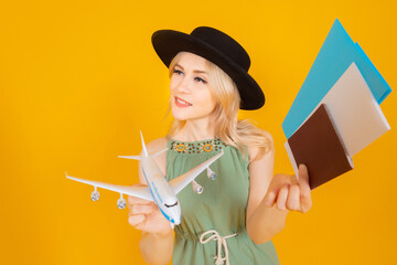 Traveler woman with a model airplane in her hands. Girl with hat on an orange background. Traveler woman demonstrates plane tickets and documents. Concept - traveler woman gathered at the airport.