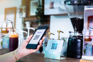 Customer hand using smart phone to scan Qr code payment tag with blurry coffee grinder in coffee shop to accepted generate digital pay without money. Qr code payment concept.