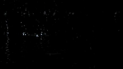 Large drops of rain fall on the black water forming rippling surface of the water. Black background. Close up. Slow motion.