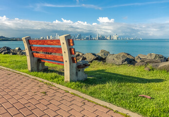 Wooden and concrete bench on the grass next to the road, overlooking the sea and the city