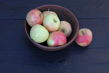 Apples in a clay cup on a dark wooden background.