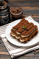 Classic tiramisu dessert and coffee grinder on ceramic plate on wooden background