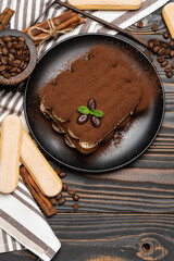 Classic tiramisu dessert on ceramic plate and savoiardi cookies on wooden background