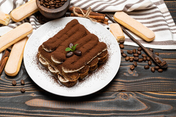 Classic tiramisu dessert on ceramic plate and savoiardi cookies on wooden background