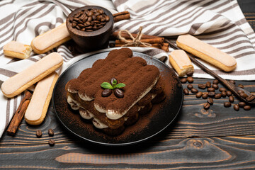 Classic tiramisu dessert on ceramic plate and savoiardi cookies on wooden background