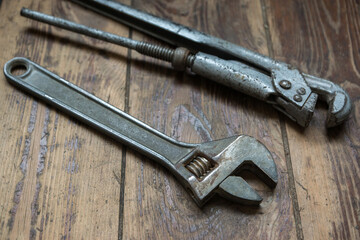 Worn out wrenches and pipe wrenches on a wooden surface. The working tool of the master for the replacement and repair of the water supply system. Selective focus, shallow depth of field