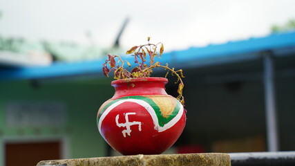 Badhal, Jaipur, India-16 March 2020; Blossoming plant in clay pot or Matka or Kalash at home on roof. Printed Swastik symbol on pot, auspicious symbol.
