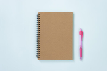 Brown Cover Spiral Notebook or Spring Notebook in Unlined Type and Pink Pen on Blue Pastel Minimalist Background. Spiral Notebook Mockup on Center Frame