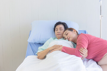 An Asian woman embraces her mother who is recuperating on a hospital bed.