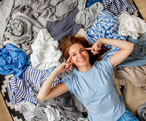 Beautiful caucasian woman smiling and lying down with clutter clothes on the floor.