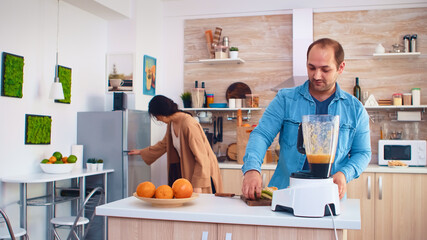 Couple mixing various fruits for nutritious and healthy smoothie in kitchen. Cheerful family making together organic healthy fresh nutritious tasty juice for breakfast from fresh fruits while on a