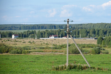 Fototapeta na wymiar Side view of a high-voltage power line laid in a field against the background of a forest and a blue sky with white clouds