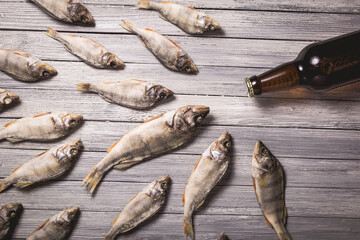 Dried perch and brown glass beer bottle on white wooden background.
