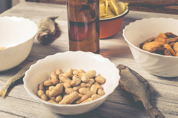 On a wooden table a bottle of beer, dried fish, chips, crackers and nuts.