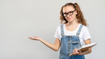 Smart student portrait. School presentation. Cheerful teen girl in eyeglasses with books showing copy space isolated on neutral background. Course promotion. Modern education. Academic class.