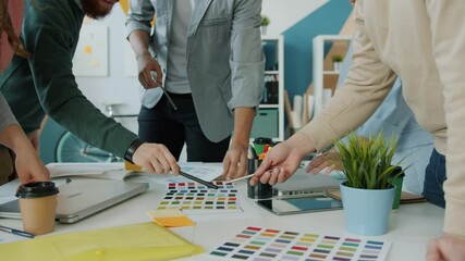 Hands of creative designers are working with color palettes during meeting in office while team of young people are discussing business ideas.
