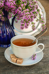 White cup of tea on thyme background on an old wooden table on a clear sunny day