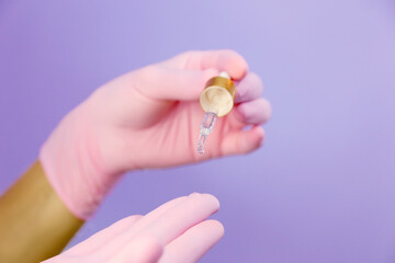 Closeup of hands in pink gloves with pipette and drop of transparent oil