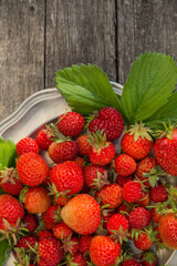 Ripe strawberries on a plate and an old wooden background on a sunny afternoon.