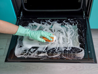 women's hands in gloves using a sponge and detergent cleans the oven door.