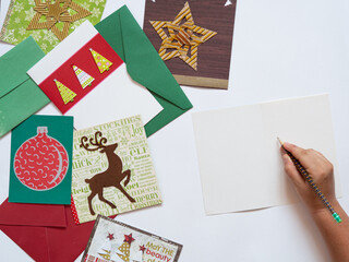 Top view of christmas letters with holiday motives as trees, reindeer and star. Caucasian hand with pencil writing for the holidays. Flat lay on white background with copy space. 
