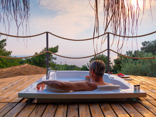 A handsome adult man lies in a hot tub at a luxurious exotic spa resort hotel balcony with sea and...