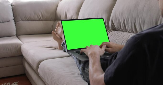 Over the shoulder shot of a businessman working in home office interior on pc MacBook Pro, looking at green screen. Office person using laptop computer with laptop green screen