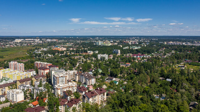 Urban buildings between green trees. Beautiful view of city downtown. Aerial view photo of cityscape and skyline at summer sunny day.