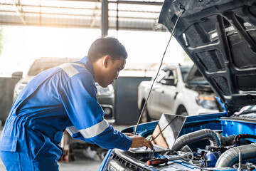 Mechanic Asian man using laptop computer examining tuning fixing repairing car engine automobile...