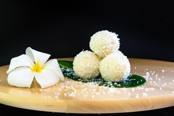coconut flakes scattered around the candy, sweet milk balls with coconut flakes and frangipani flower for decoration, oriental sweets on a green leaf