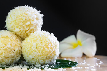 sweet milk balls with coconut chips close up, oriental sweets on a green leaf with frangipani flower