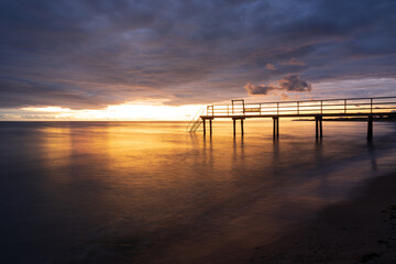 Fototapeta na wymiar Bathing jetty with reflection in the sea during golden sunset in south Sweden. Selective focus.