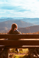 Fototapeta na wymiar A lonely girl sits on a bench and enjoys the stunning view of the autumn mountains